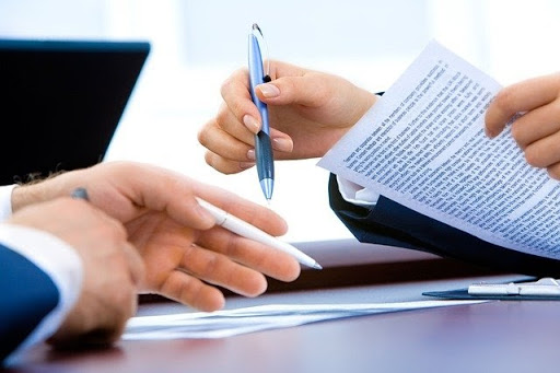 Two pairs of hands resting on a table, with professional documents and one person holding a pen.